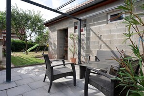 Een terras buiten met rieten meubels, een potplant en een stenen muur.