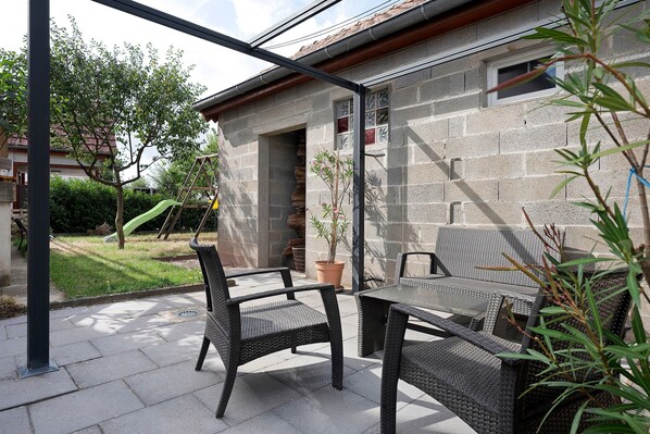 An outdoor patio with wicker furniture, a potted plant, and a stone wall.