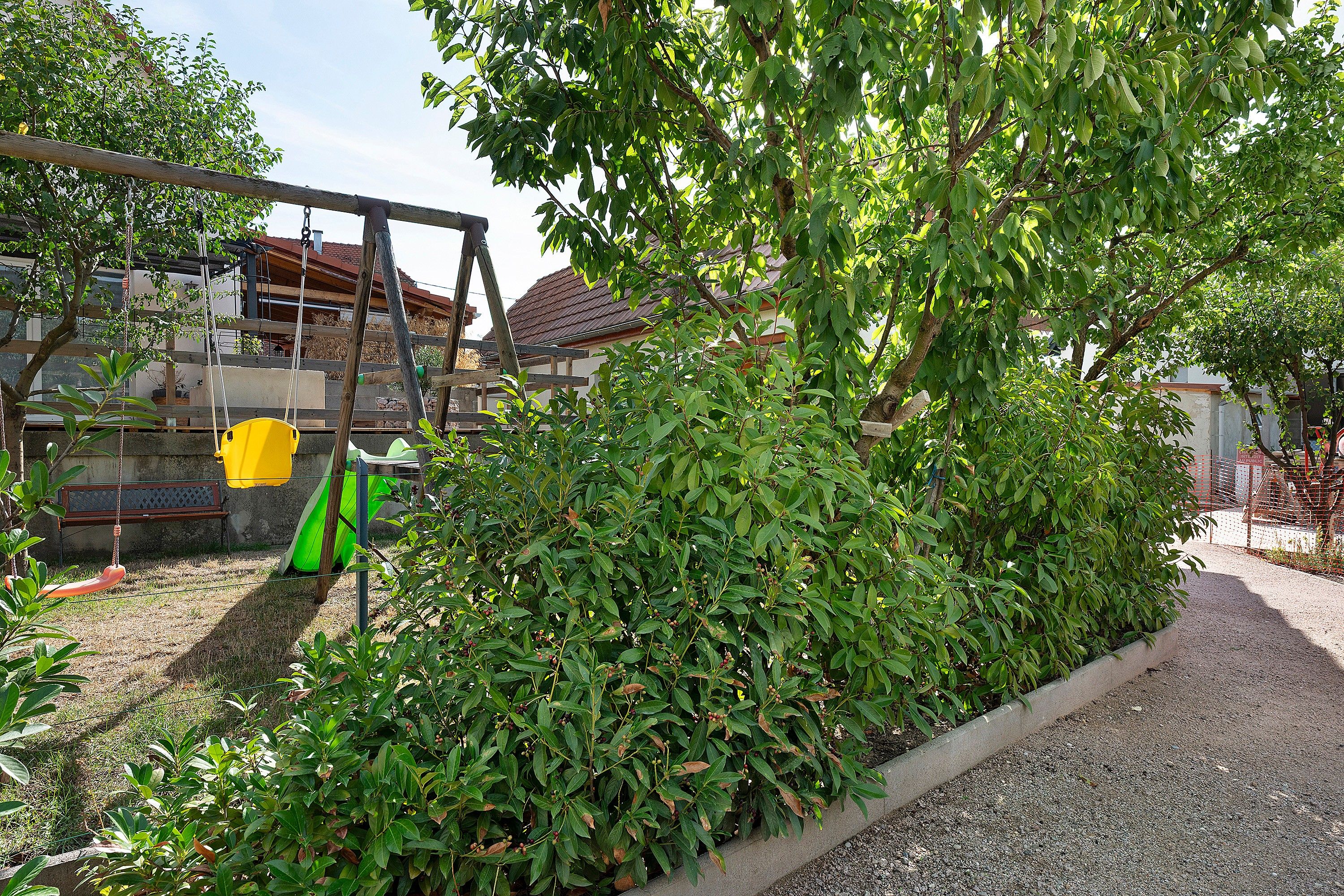 A garden area with a swing set, a bench, and a hedge.