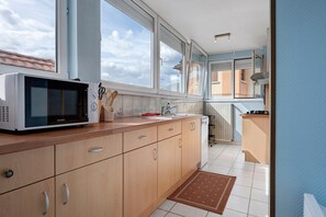 A modern kitchen with wooden cabinets, a microwave, and a view of the outside through large windows. - Les bleuets - at Rosine and Pierre's, Alsace charm near Scherwiller vineyards (Châtenois)
