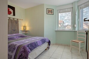 A bedroom with a bed, a chair, a window, and a wall-mounted light fixture.