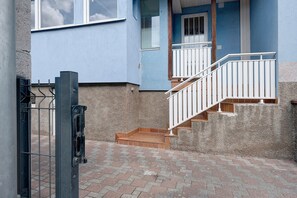 A residential building with a blue exterior, a gated entrance, and a staircase leading to a balcony.