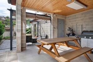 Un patio exterior con mesa y banco de madera, una parrilla de barbacoa y una pared de piedra.