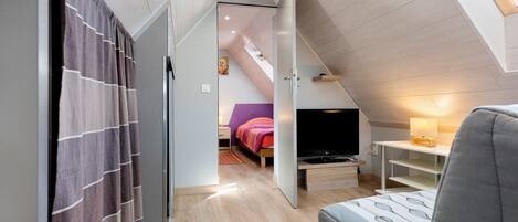 A modern bedroom with a sloped ceiling, a bed with a colorful blanket, a TV, and a desk with a lamp.