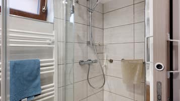 Een douche met een glazen deur, een handdoekhouder met een blauwe handdoek en een douchekop.