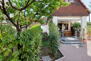 Il s’agit d’une propriété résidentielle dotée d’un porche abrité, d’un escalier menant à une terrasse en bois et d’un jardin agrémenté de diverses plantes.