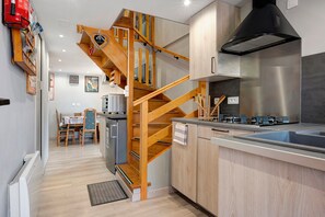 Une cuisine moderne avec un escalier en bois, des appareils électroménagers en acier inoxydable et un coin repas comprenant une table et des chaises.