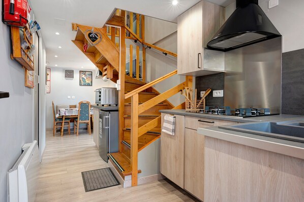 A modern kitchen with a wooden staircase, stainless steel appliances, and a dining area with a table and chairs.