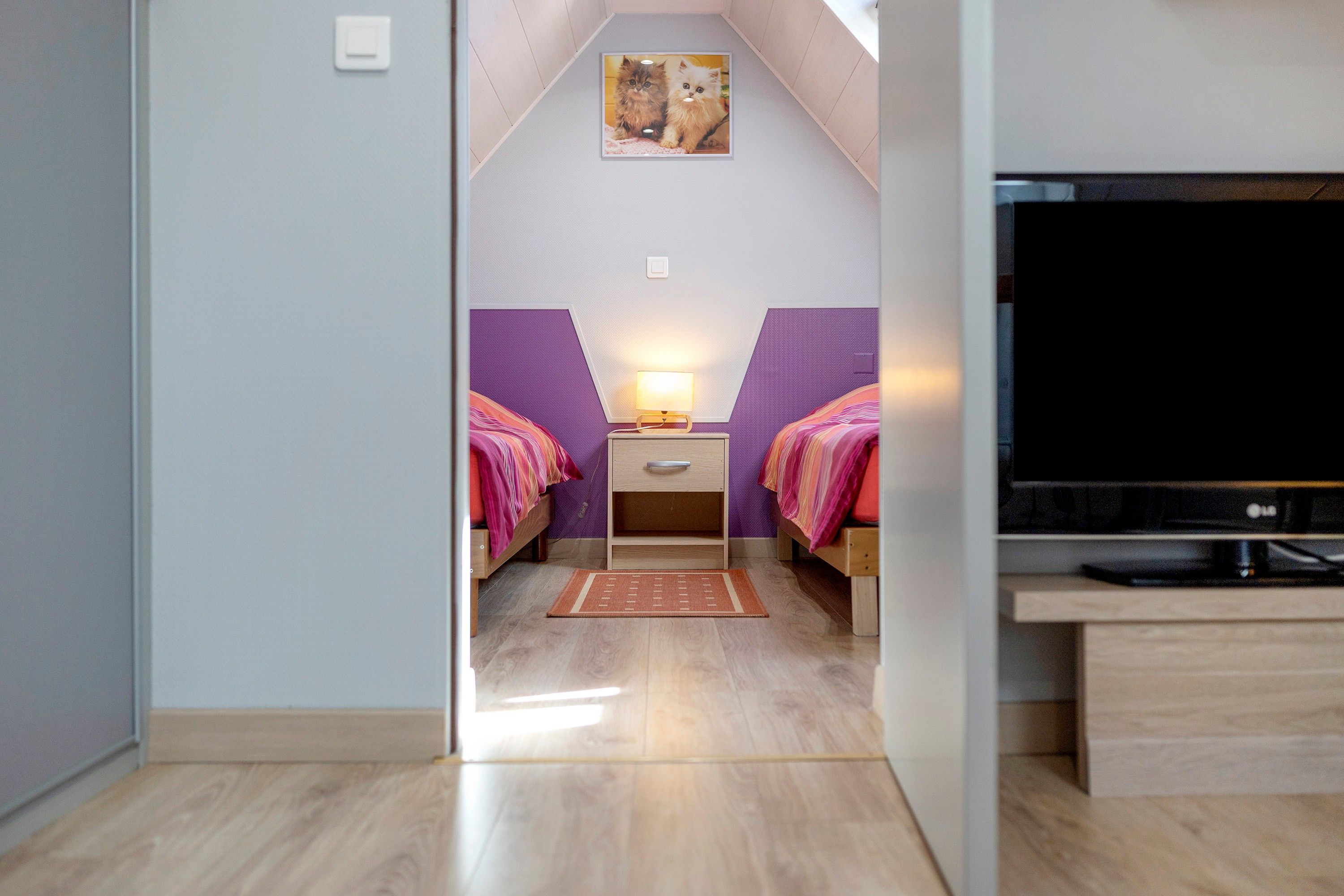 Een slaapkamer met twee bedden, een televisie en een klein tafeltje met een lamp.