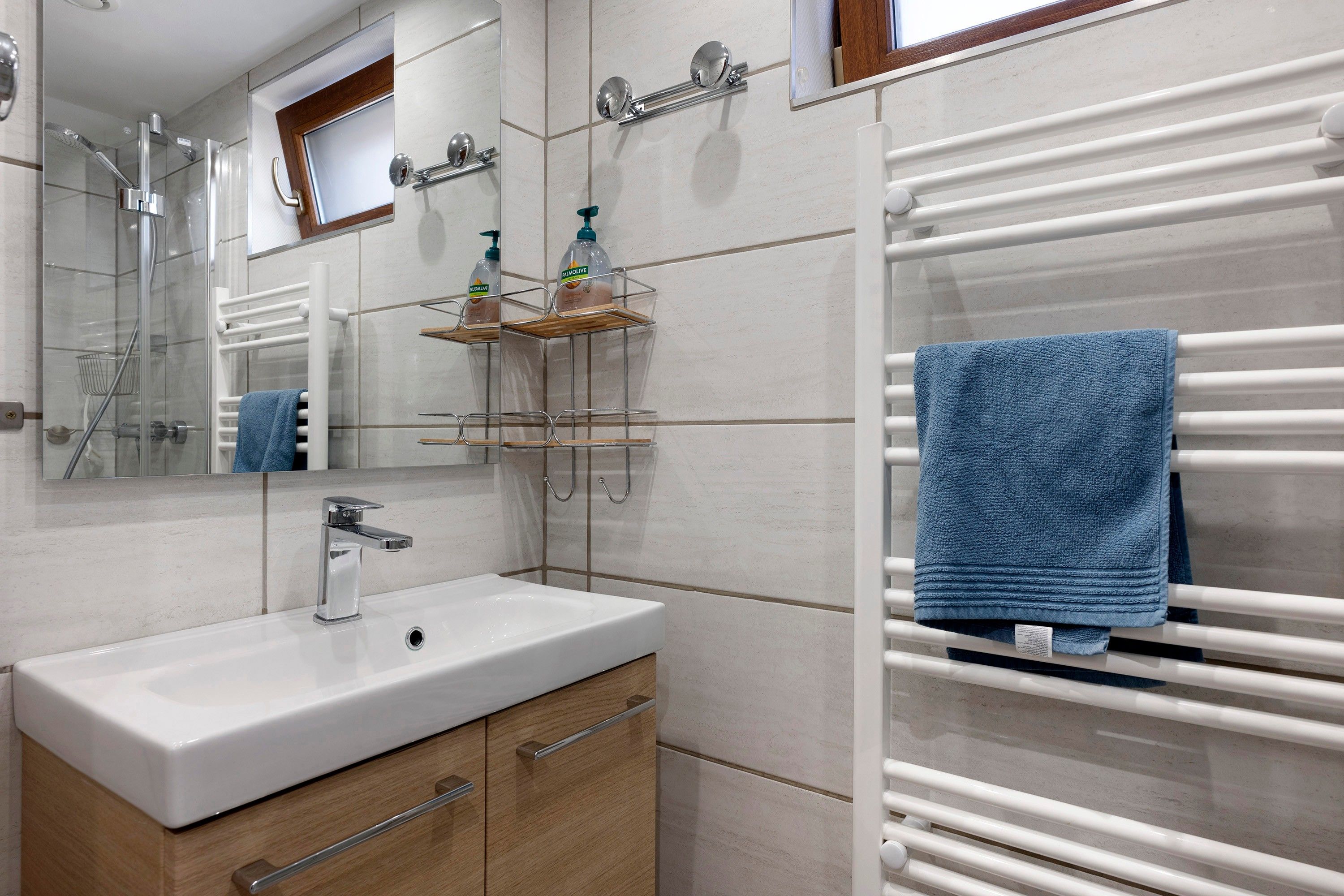 Uma casa de banho moderna com lavatório branco, espelho, porta-toalhas e chuveiro.