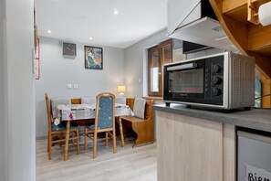 A compact kitchen with a microwave, wooden cabinets, and a dining area with a table and chairs.