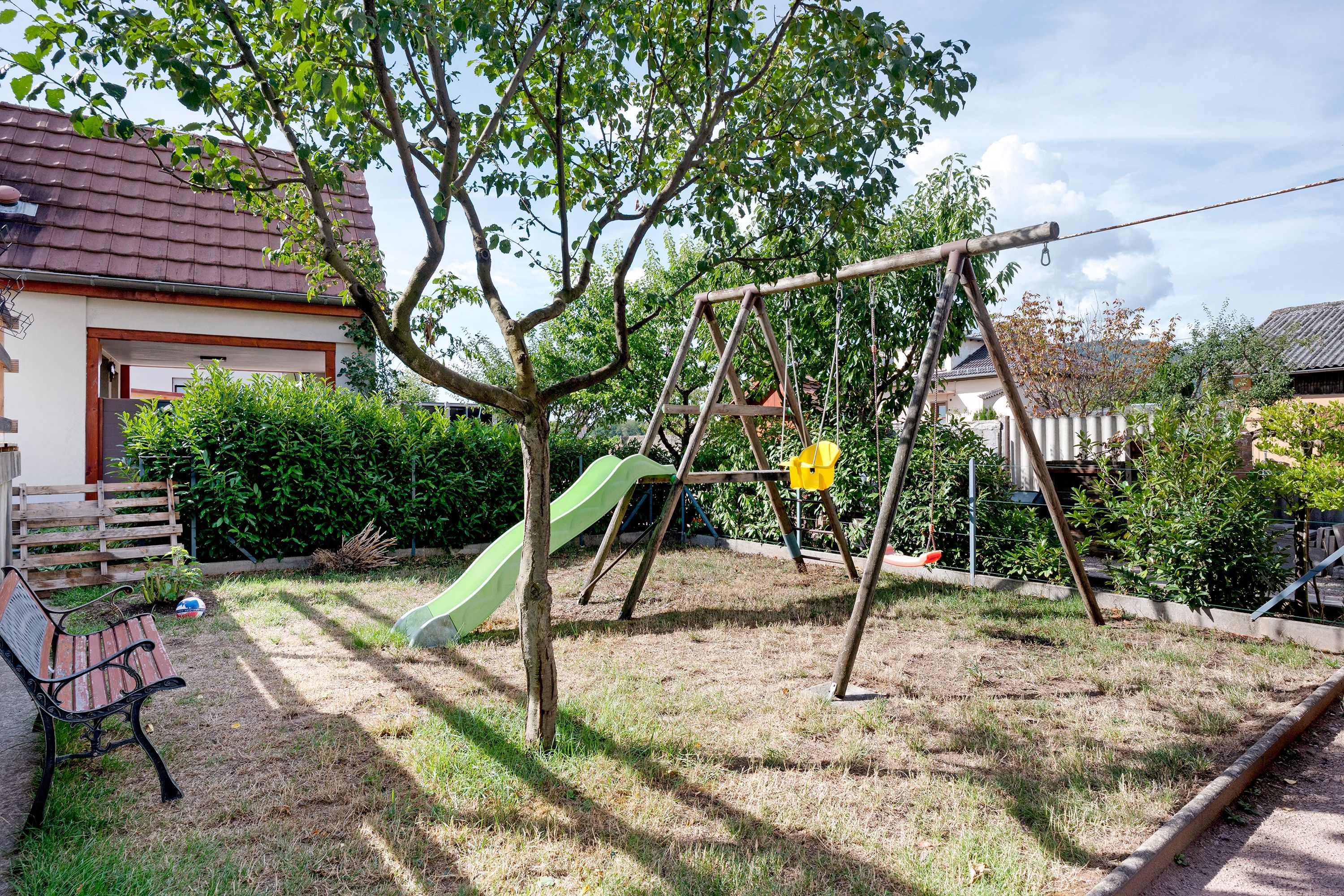 Een speeltuin met een glijbaan en schommels, omgeven door gras en bomen.