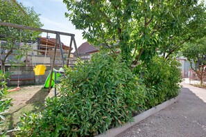 A garden area with a swing set, a bench, and a hedge.