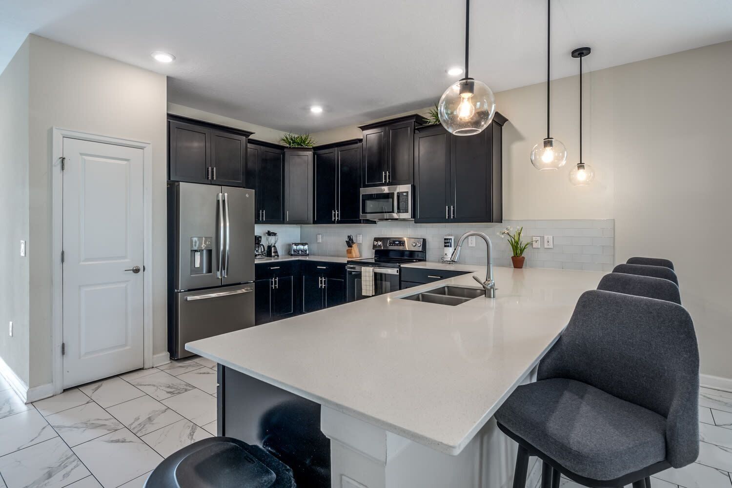 A modern kitchen with dark cabinets, stainless steel appliances, a large island with seating, and pendant lighting.