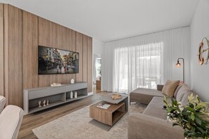 A modern living room with a flat-screen TV mounted on a wooden wall, a sofa set, a coffee table, and a sideboard with decorative items. - Modern 5BR Home Near Disney with Private Pool (Kissimmee)