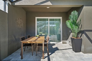 A patio with a wooden table and chairs, a potted plant, and a sliding glass door leading to a garden. - Modern 5BR Home Near Disney with Private Pool (Kissimmee)