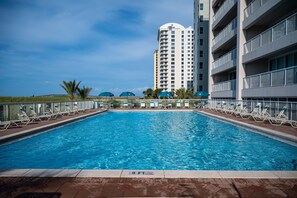 A swimming pool with lounge chairs and umbrellas, surrounded by a fence, with a tall building in the background. - Regency 308 -NEW LISTING AS OF AUGUST 2026! Sea You on the Flip Tide! (Navarre)