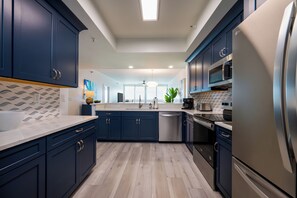 Une cuisine moderne avec des meubles de couleur bleu foncé, des appareils en acier inoxydable et un plancher en bois clair.