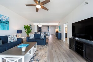 A modern living room with a ceiling fan, a flat-screen TV, and a dining area in the background. - Regency 308 -NEW LISTING AS OF AUGUST 2026! Sea You on the Flip Tide! (Navarre)