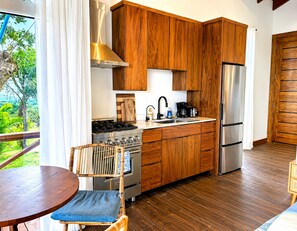A modern kitchen with wooden cabinets, stainless steel appliances, and a view of greenery outside. - Suite Perspective – Private Hilltop Casita with Pool (Punta Blanca)