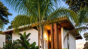 Ein Haus mit weißer Fassade, einer Holzterrasse und einem gepflegten Garten mit verschiedenen Pflanzen und einer Palme.