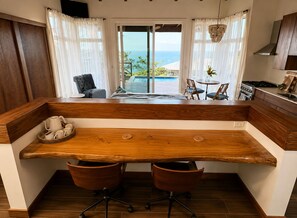 A modern kitchen with a wooden island, two chairs, and a view of the ocean. - Suite Perspective – Private Hilltop Casita with Pool (Punta Blanca)