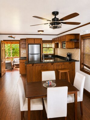 A modern kitchen with wooden cabinets, a stainless steel refrigerator, and a dining area with a table and chairs. - Seas the Day-Oceanfront 2 Bedroom Water Access Only (Oakridge)