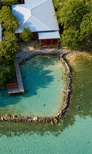Eine Vogelperspektive auf ein Resort mit einem klaren, blauen Pool, einer Holzterrasse und einem Gebäude mit blauem Dach.