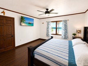 Ein Schlafzimmer mit einem Bett, einem Deckenventilator, einem Fenster mit Vorhängen, einem Bild an der Wand und einer Tür.