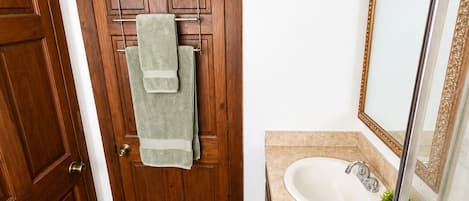 A bathroom with a wooden door, a towel rack with two towels, a sink with a mirror, and a small rug on the floor.