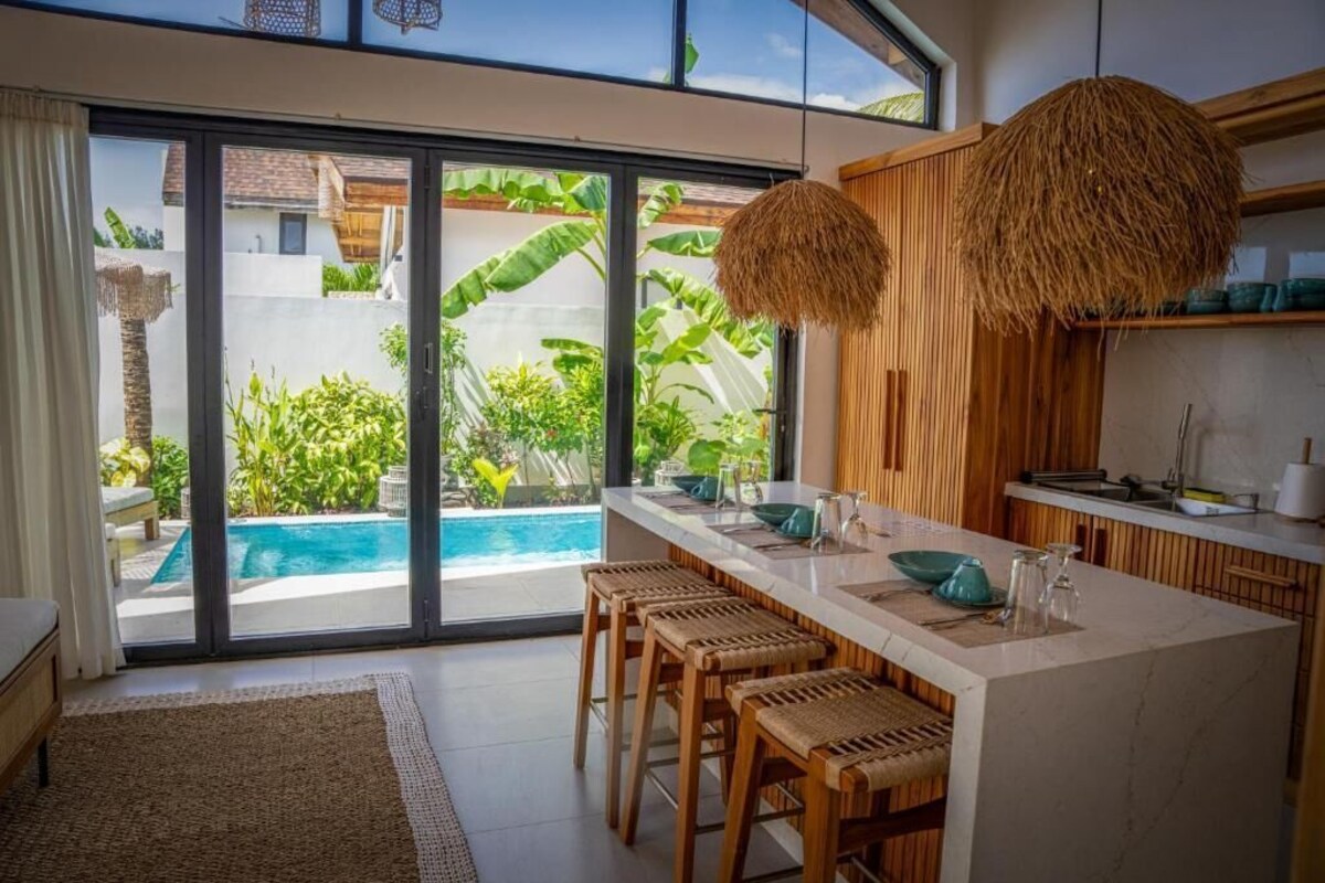 A modern kitchen with a large island, bar stools, and a view of a pool.