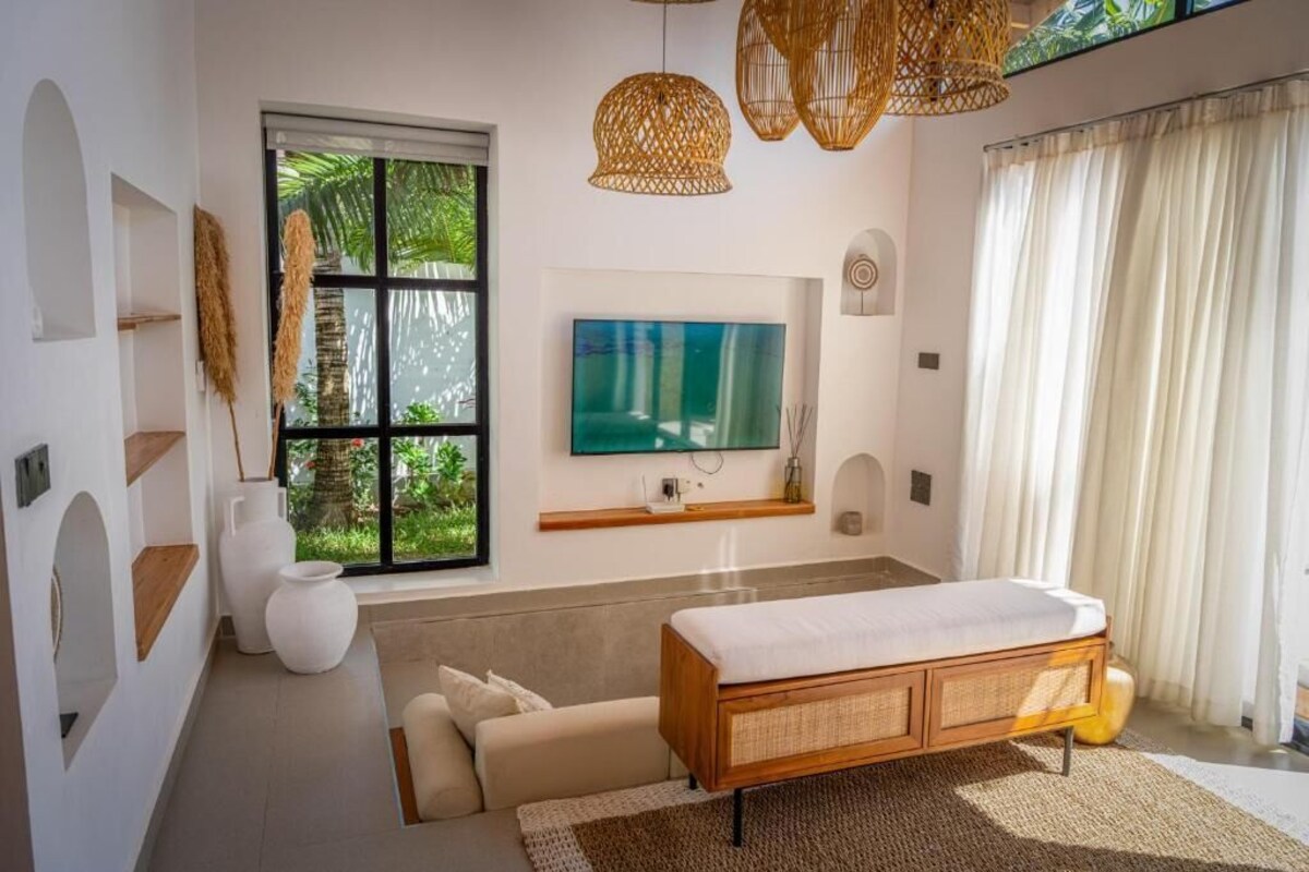 A modern bedroom with a bed, a TV, and a window with a view of greenery.