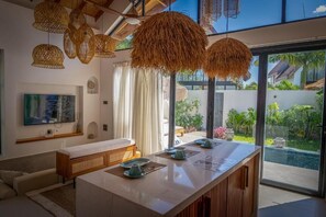 A modern interior with a long dining table, hanging wicker lamps, and a view of a swimming pool and greenery. - Paje Emerald Escapes (Zanzibar)