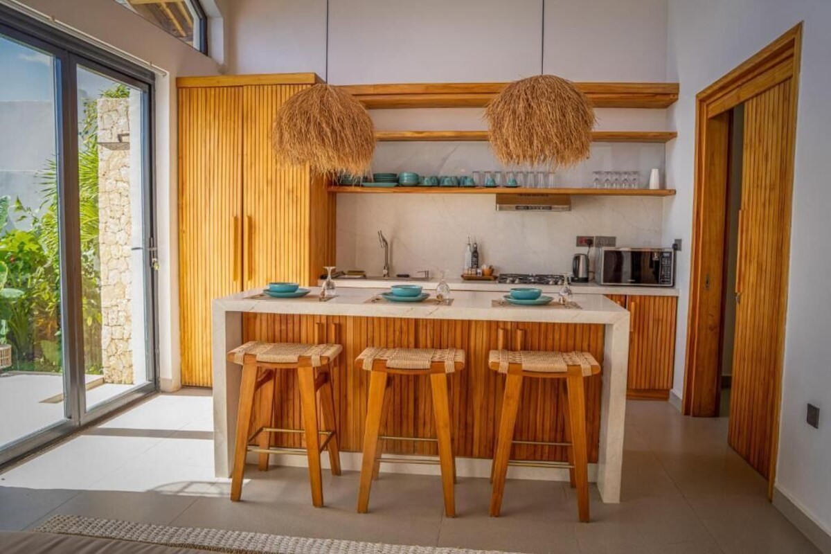 A modern kitchen with a central island, wooden stools, and hanging light fixtures.