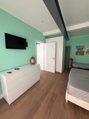 A bedroom with a bed, a dresser, a television mounted on the wall, and a door leading to another room. - Chioggia: Between the Sea, History, and Tradition (Chioggia)