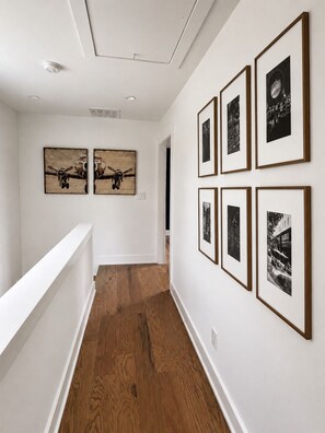 A hallway with wooden flooring, white walls, and framed black-and-white photographs. - The Breakspear House - 4BR Trilith Stay for Production & Soccer in Fayetteville (Fayetteville)