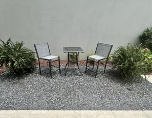 Ein Sitzbereich im Freien mit zwei Stühlen und einem Tisch, umgeben von Kies und Pflanzen.