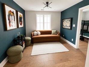 A living room with a brown sofa, a white rug, a round ottoman, and a framed map on the wall. - The Breakspear House - 4BR Trilith Stay for Production & Soccer in Fayetteville (Fayetteville)