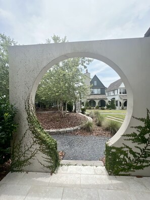 A view through an arched doorway of a landscaped area with a gravel path leading to a house with a dark roof and multiple windows. - The Breakspear House - 4BR Trilith Stay for Production & Soccer in Fayetteville (Fayetteville)