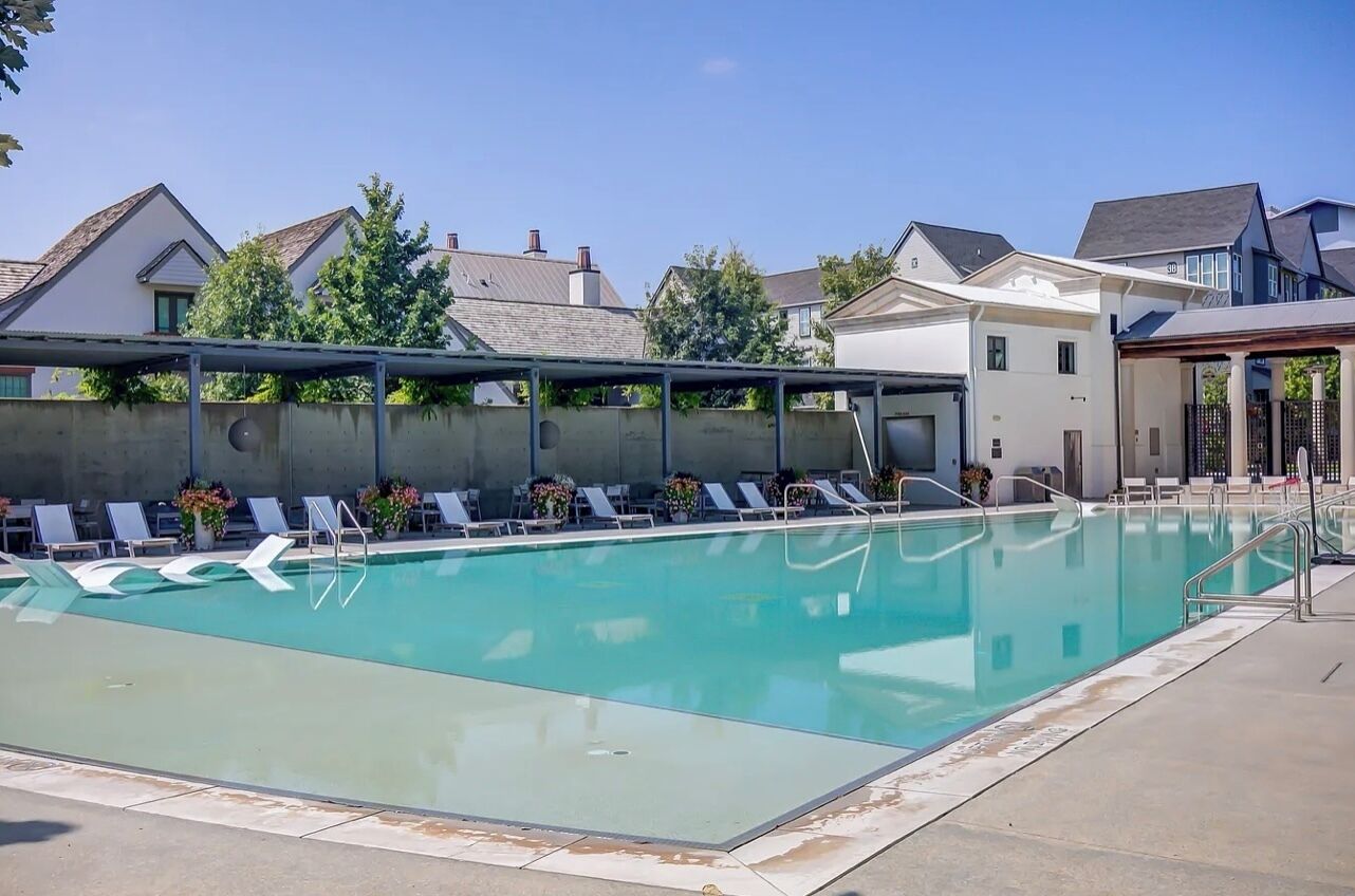 A swimming pool with lounge chairs and a covered area, surrounded by residential buildings.