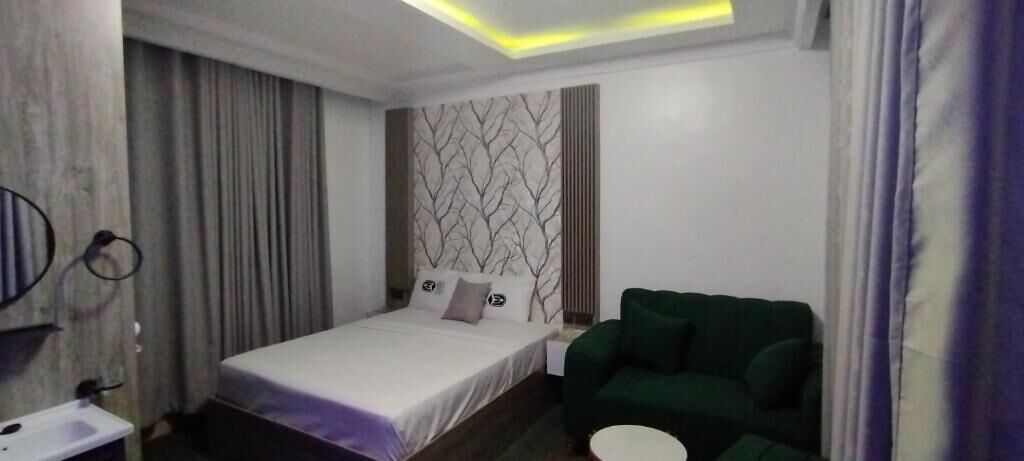 Una habitación de hotel con una cama, un sofá verde, una mesita de noche y una pared con diseño de hojas.