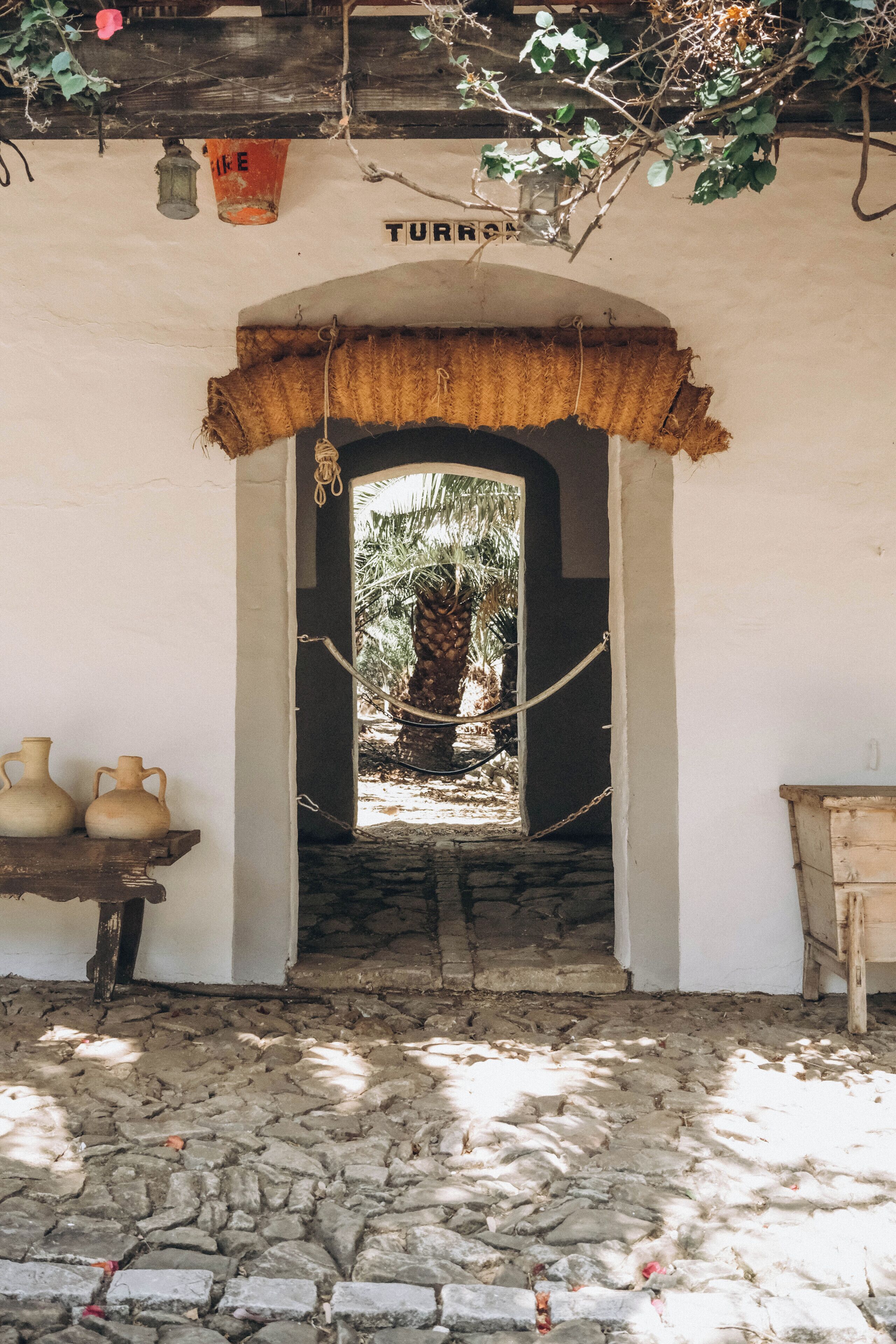 A doorway leading to a stone-paved area with a rustic wooden table and two ceramic pots.