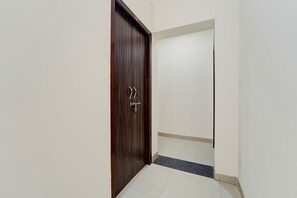 A hallway with a wooden door, a tiled floor, and a white wall.