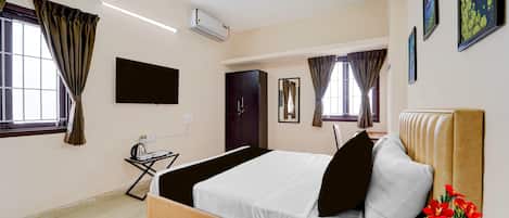 A hotel room with a bed, a desk, an air conditioning unit, a ceiling fan, and a window with curtains.