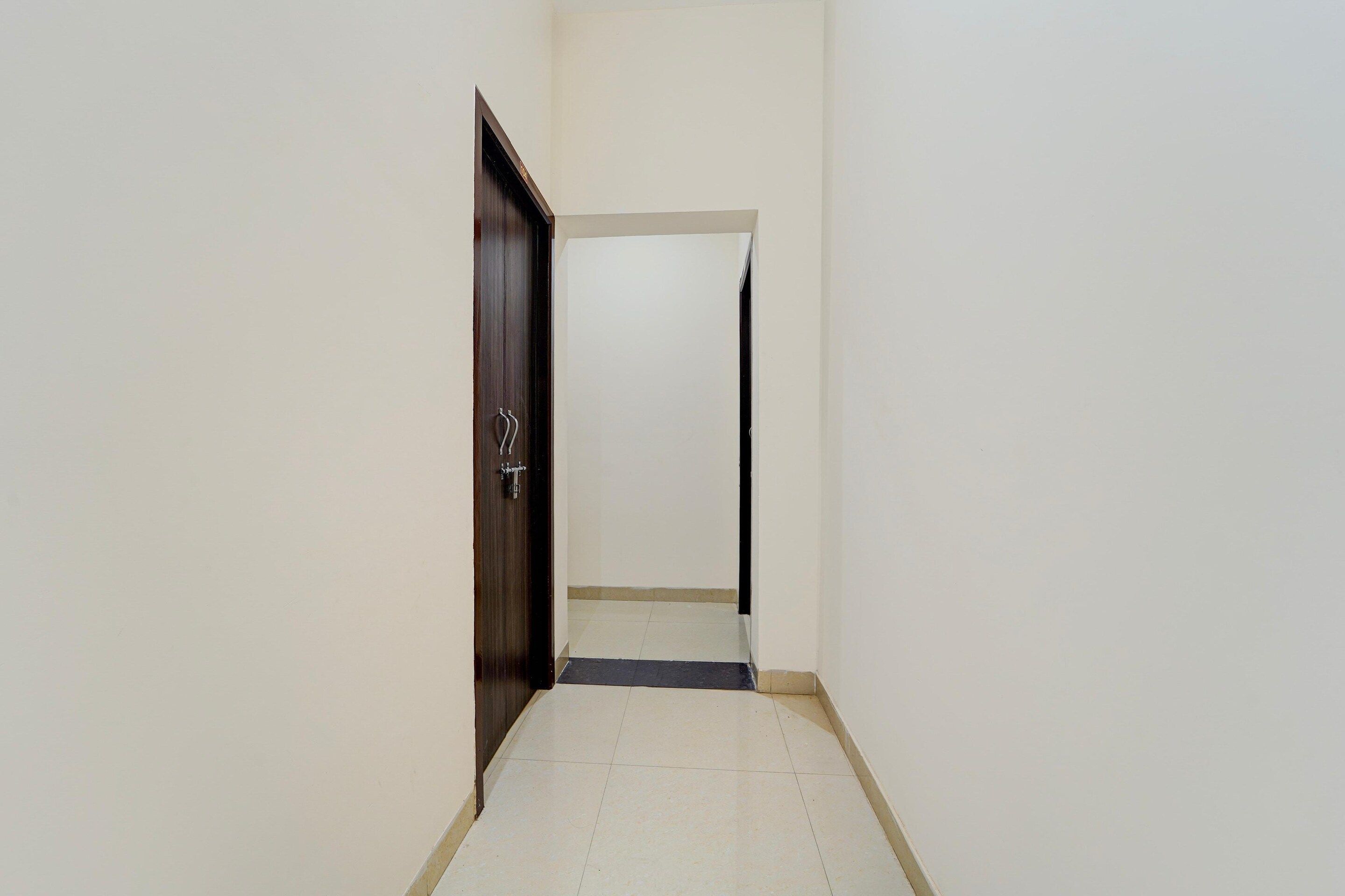 A narrow hallway with a dark wooden door on the left and a white door at the end.