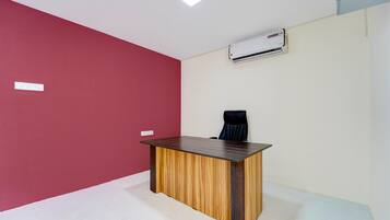 A room with a wooden desk, a black office chair, a white air conditioning unit on the wall, and a red accent wall.