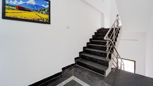 A staircase with a metal handrail leading to a landing, a framed painting of a mountain landscape, and a white wall.