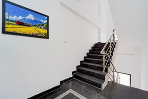 Una escalera con barandilla metálica que lleva a una plataforma, un cuadro enmarcado de un paisaje montañoso, y una pared blanca.