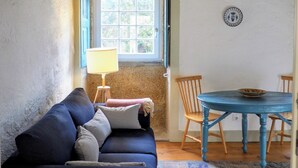 Une pièce confortable avec un canapé bleu, une petite table entourée de chaises, une fenêtre donnant sur un beau paysage et une lampe.