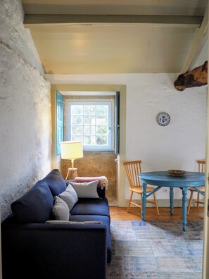Ein gemütliches Zimmer mit einem blauen Sofa, einem kleinen Tisch mit Stühlen, einem Fenster mit Blick und einer Lampe.